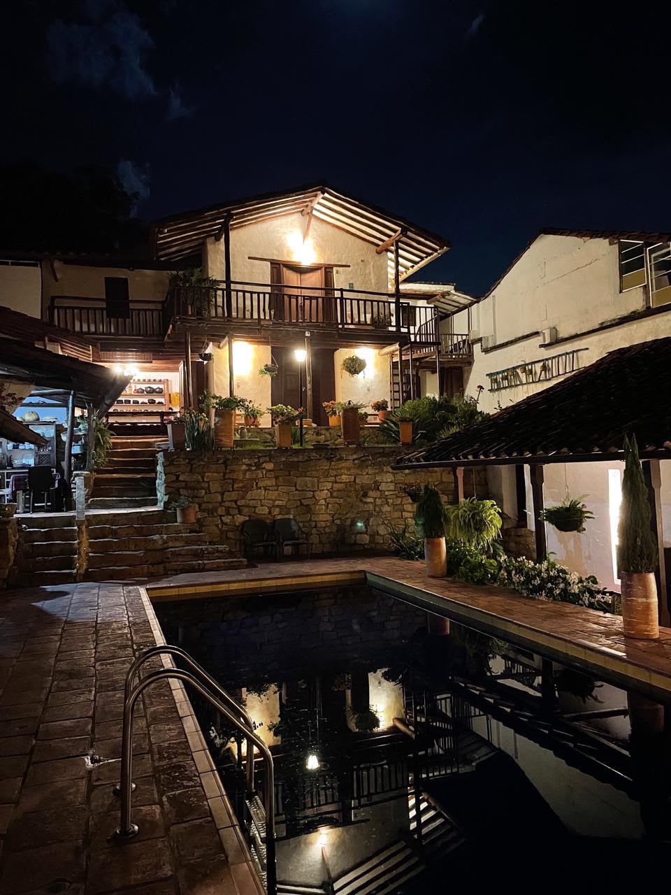 La piscina iluminada de noche, con la casa de dos pisos y sus balcones reflejados en el agua.